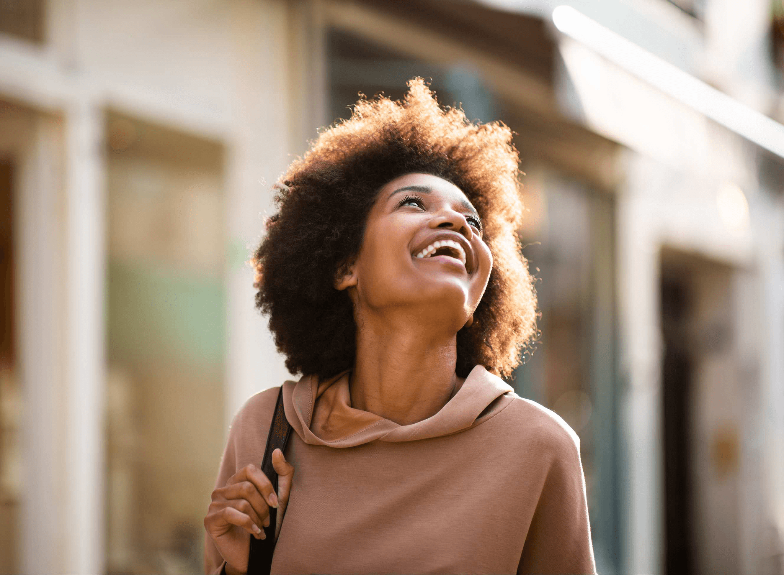 A woman laughing outdoors on a sunlit street