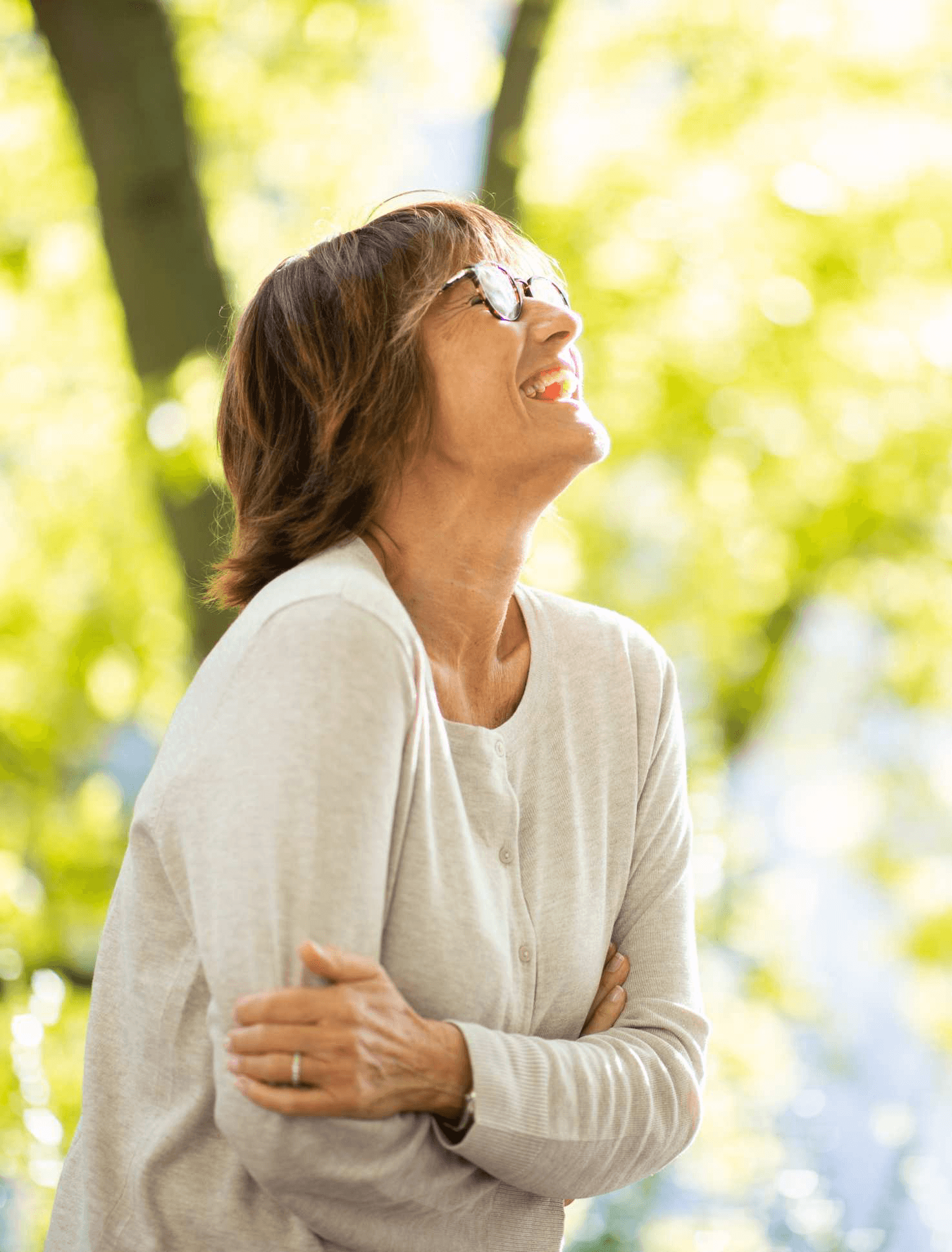 A woman standing among trees with sunlight falling through the branches
